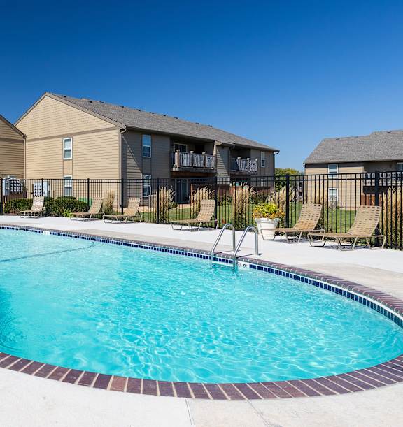 A sparkling swimming pool at Cedar Crest Apartments, surrounded by lounge chairs and lush landscaping.